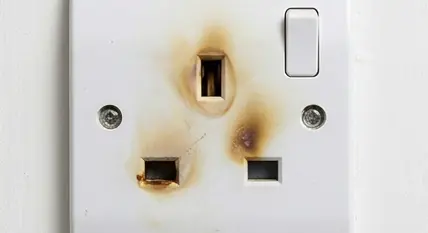 UK plug socket with brown burn marks around the pin holes — a sign of electrical arcing that requires immediate professional attention